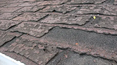 Close-up of worn, curling and cracked asphalt shingles on a residential roof