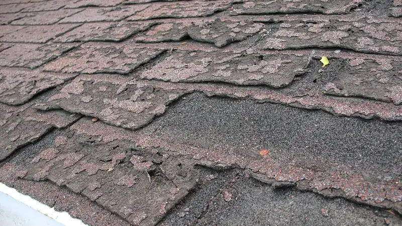 Close-up of worn, curling and cracked asphalt shingles on a residential roof